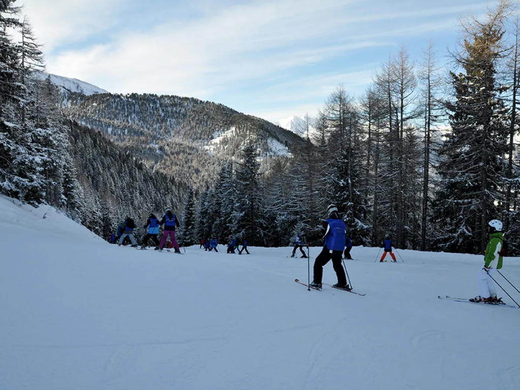 Skifahrende auf einem breiten Hang unter blauem Himmel.